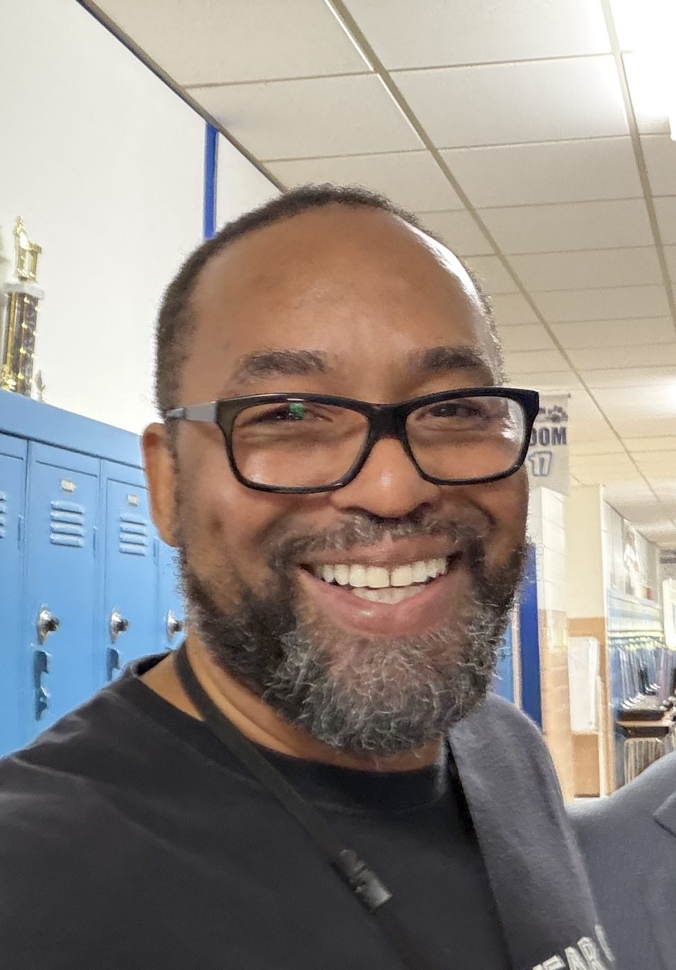 Eli M. Davis smiling in a school hallway with blue lockers and a trophy case