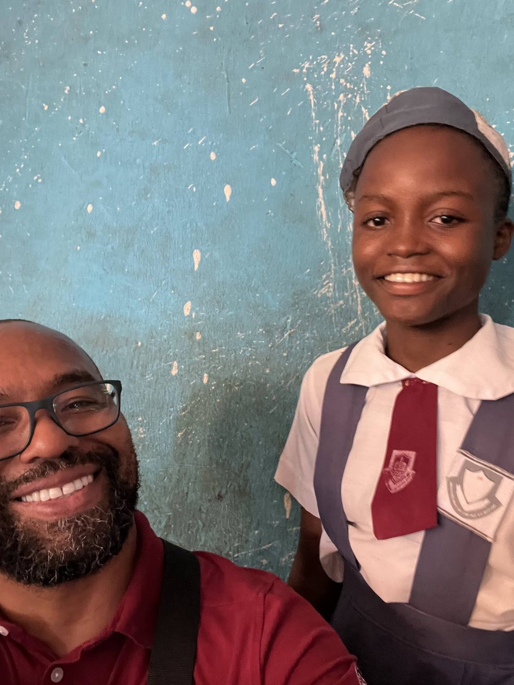 Eli Davis smiling beside a student in uniform against a blue classroom wall in Nigeria